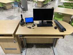 Top down view of the instructor’s podium. The podium is equipped with a computer, a document camera and a set of microphones.
