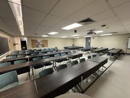 View of the classroom from the instructor’s podium. There are four rows of tables with chairs for students. A blackboard is located on the right wall. This classroom is not accessible for instructors. The podium is equipped with a document camera, lecture capture and a set of microphones.