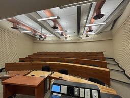 View of the classroom from the instructor’s area at the front. There are multiple rows of long curved tables and chairs for students. This classroom is accessible for instructors.
