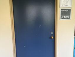 The entryway of room A309 in Mackintosh Corry Hall is a blue door with a doorknob on the right side.