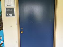 The entryway of room A311 in Mackintosh Corry Hall is a blue door with a doorknob on the left side.