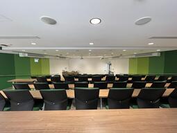 View of the classroom from a student seat near the rear of the room. The podium is at the front of the room on the left. When presenting, the image is projected on the wall to the right of the instructor’s podium.