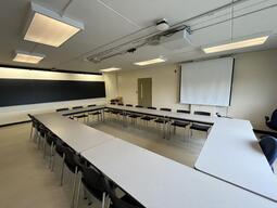 View of the classroom from the front of the classroom There are multiple tables and chairs for students, arranged in a rectangle in the centre of the room. The entryway door is located on the right side of the classroom. The instructor’s podium is located at the back of the room, on the right. This classroom is accessible for instructors.