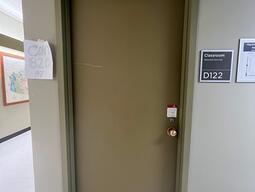 The entryway of room D122 in Mackintosh Corry Hall is a brown door with a doorknob on the right side.