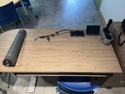 Top-down view of the podium. The podium has a set of microphones, document camera, and set of display cables. The podium is height adjustable and accessible.