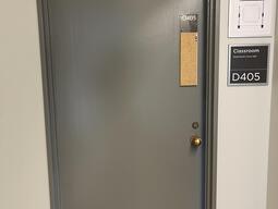 The entryway of room D405 in Mackintosh Corry Hall is a grey door with a silver doorknob on the right side.