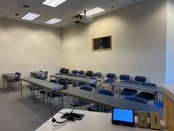 View of the classroom from the instructor’s podium. There are two rows of tables and chairs for students. This classroom is accessible for instructors.