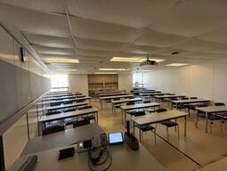 View of the classroom from the instructor’s podium. There are six rows of long tables and chairs for students. This classroom is not accessible for instructors.