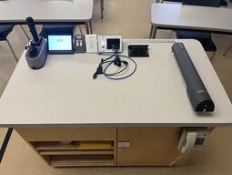 Top-down view of the podium. The podium is equipped with a document camera, lecture capture, a set of microphones and connection cords to project media.