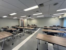 View of the classroom from the instructor's podium. In front are rows of movable tables and chairs. The door is located at the left. Chairs and tables are movable to fit the instructors needs. The classroom is accessible for instructors.
