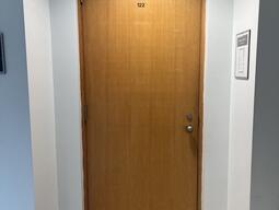 The entryway of room 122 in Watson Hall is a wooden door with a doorknob on the right side.