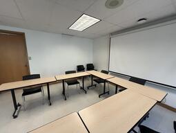 View of the classroom from the instructor’s podium. There are multiple desks and chairs for students, arranged in a rectangle in the centre of the room. A blackboard is located at the back of the classroom. This classroom is accessible for instructors.