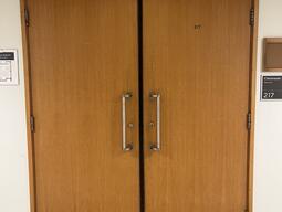 The entryway of room 217 in Watson Hall is a wooden double door with silver handles on each door.