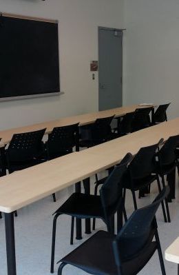 2 rows of small tables with black chairs facing a blackboard