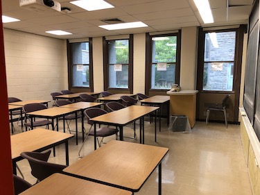 Classroom with movable tables and tables and a row of windows in the background.