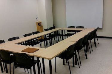 Small seminar room with narrow tables put together in the shape of a rectangle with moveable chairs