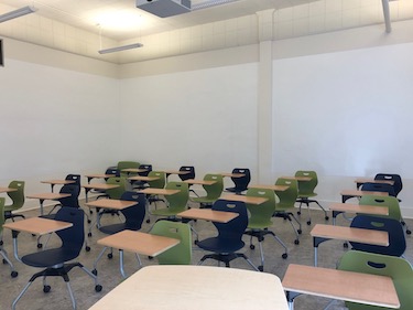 Instructor view of classroom with blue and green movable chairs and whiteboard surface on all walls. 