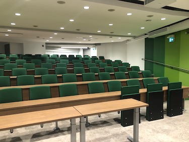 Classroom view from the front of room with green chairs and narrow light wood tables.