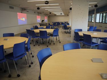 View from the side of the room: Round tables with moveable chairs. There are whiteboards along the sides of the room. 