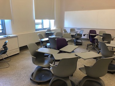 View from the side of the room: Moveable chairs with attached tablet tables in a room with beige walls.