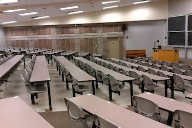 View from the back of the room: Rows of fixed tables with chairs attached with grey walls