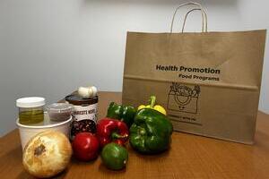 Paper bag with green, red, yellow peppers, an onion, and various spice containers on a wood table