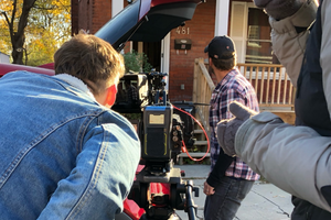 Man in jean jacket looking into a camera pointed at a front porch(taken from behind)