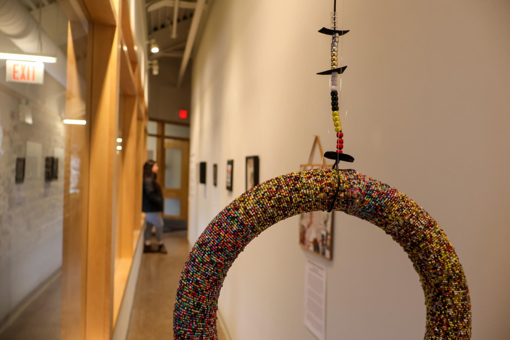 A textured and colourful large ring hanging from a beaded string in an art gallery.