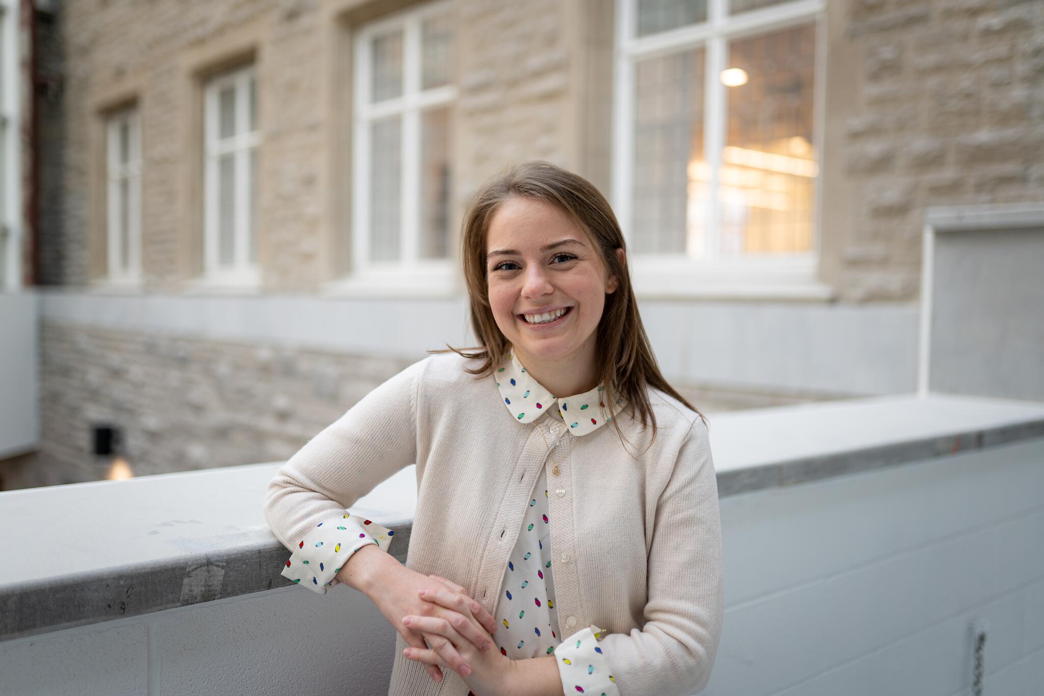 Young woman with shoulder-length hair in a white blouse with a beige cardigan partially covering it.