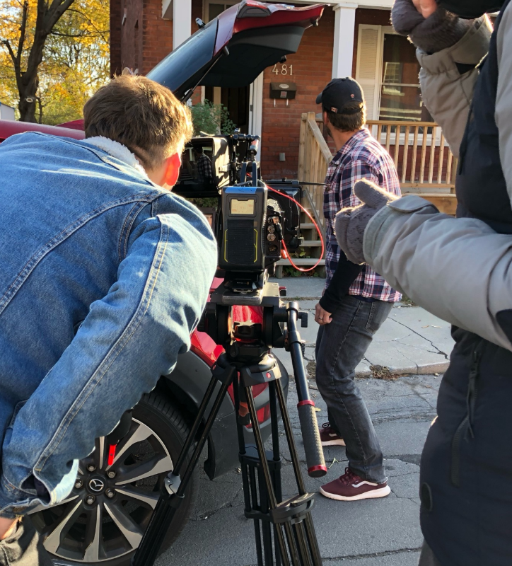 man in jean jacket looking into a camera pointed at a front porch(taken from behind)
