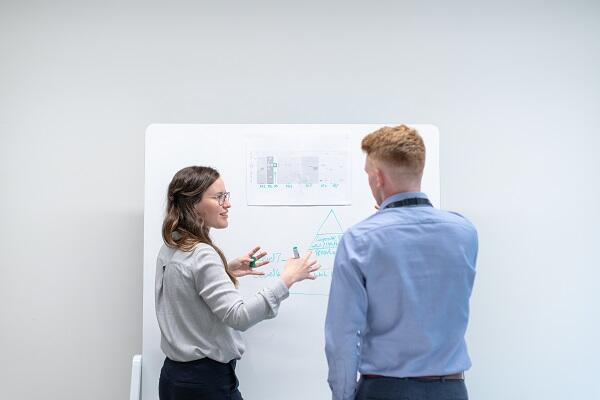a woman and man talking infront of a board with papers on it