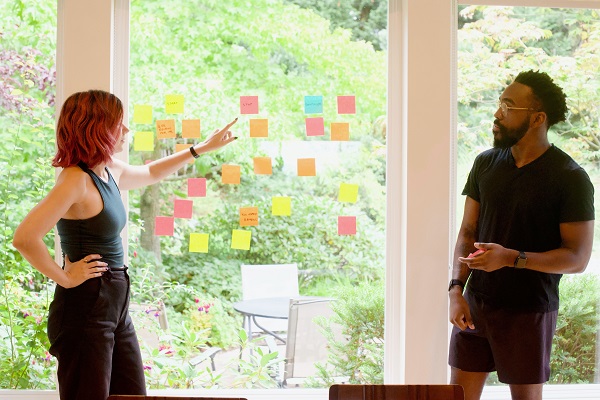 a man and a woman standing, reviewing post-its on a window