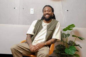 Photo of Christopher Wilson sitting on a chair smiling.