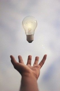 A hand reaching out to catch a light bulb that is turned on