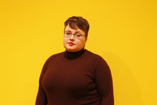 A woman stands against a yellow background