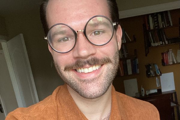 Photo of Jesse smiling in button-down shirt and round black glasses