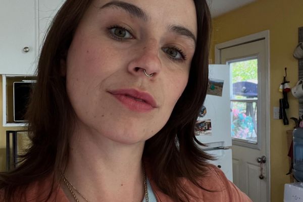 young woman with brown hair, wearing a coral shirt 