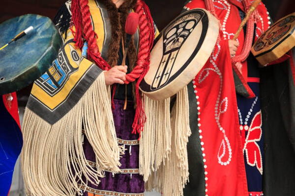 Indigenous person in traditional clothing holding drums