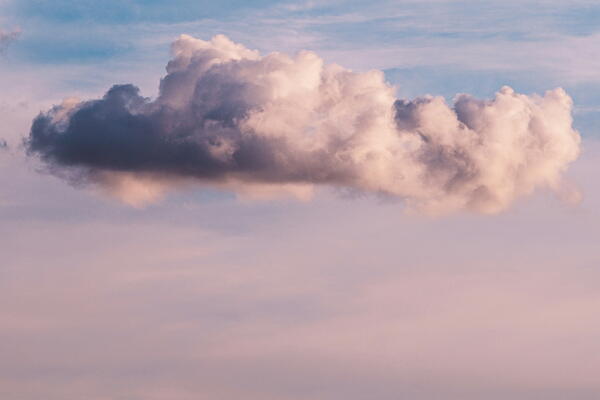 Photograph of a single fluffy cloud floating against a gradient sky transitioning from soft pink near horizon to bright blue above.