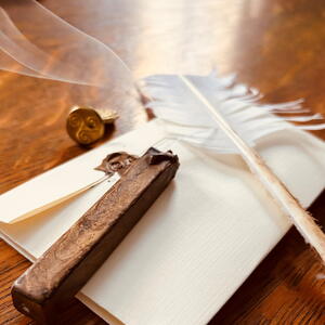 Photograph of vintage writing tools arranged on a wooden surface, including a white feather quill, sealed envelopes with wax stamps, and a smoking incense stick in a carved holder. The composition highlights historical communication methods with warm lighting emphasizing textures of paper, wax, and wood.