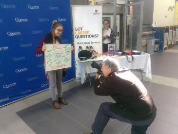 Laura Wyatt holding an It All Adds Up board and being photographed by a reporter during the 2016-17 It All Adds Up Campaign
