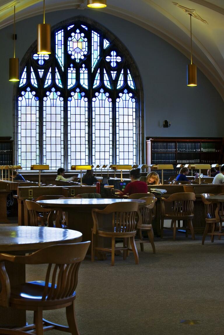 Inside library space - tables, chairs, students and a stained glass window