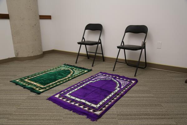 Two folding chairs placed behind prayer rugs, one green, other is purple in the prayer and meditation room at the School of Medicine. Go to campus map.
