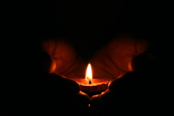 two hands in the dark holding a lit candle