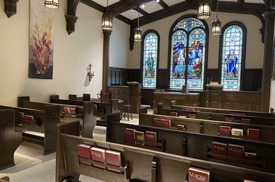 A chapel with rows of pews and artistic renditions of biblical figures in the windows