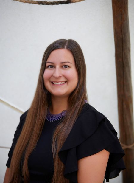 a photo of a woman sitting in a tipi. she is wearing a black top and smiling. she is wearing a purple beaded necklace