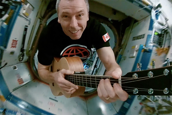 Astronaut Drew Feustel playing a guitar while floating through the International Space Station.