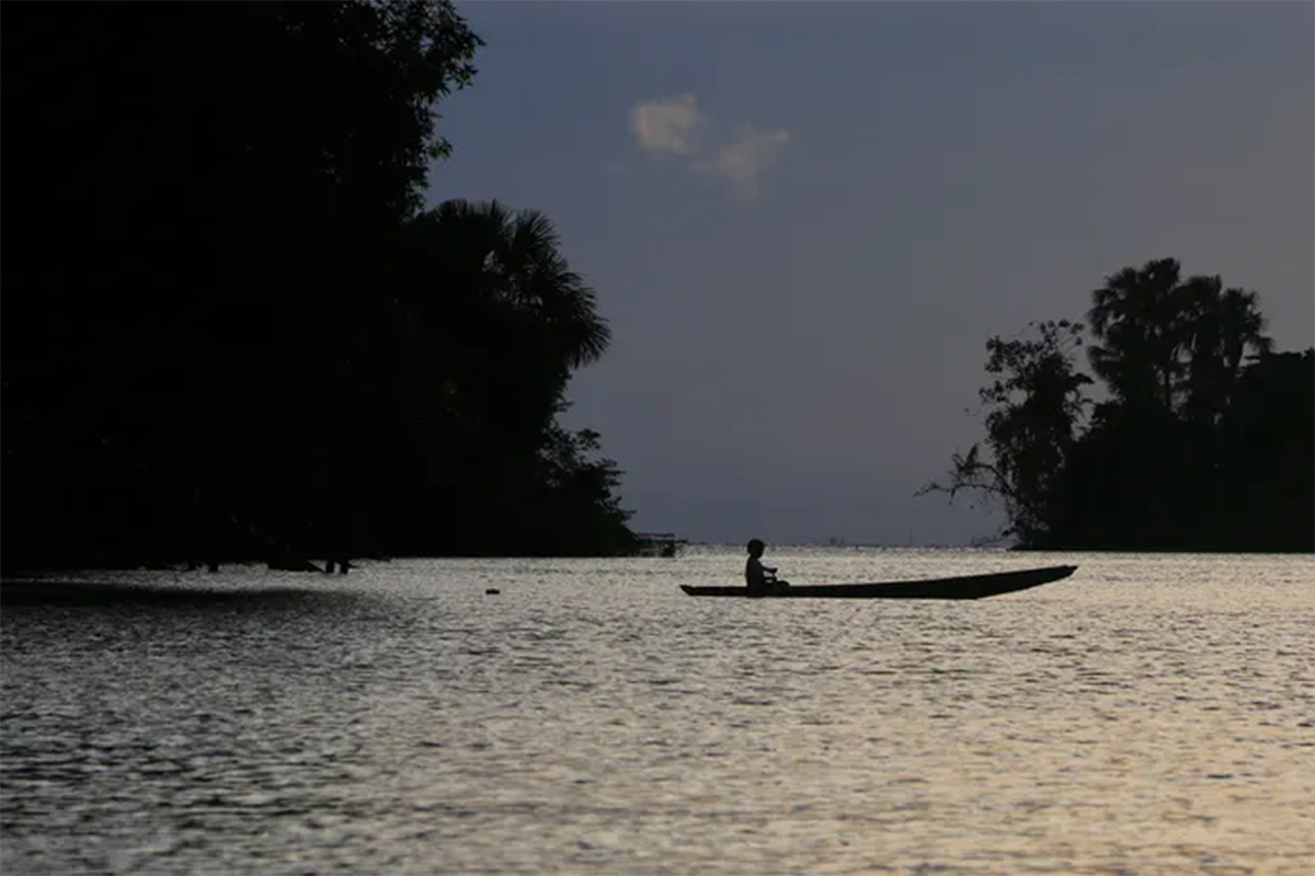 A Brazilian boy in a dugout canoe crosses a river in the evening.