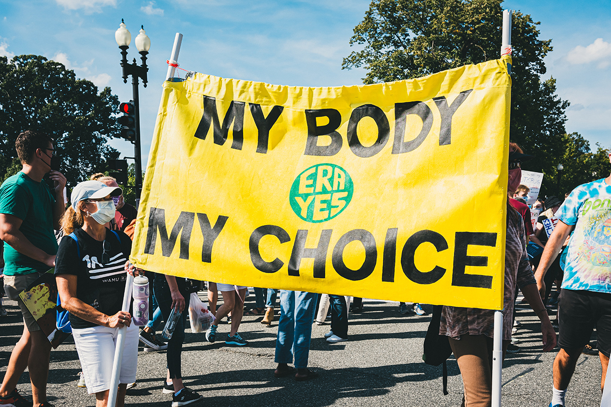 Women hold up a yellow sign with 'My body, my choice' on it in black letters. 