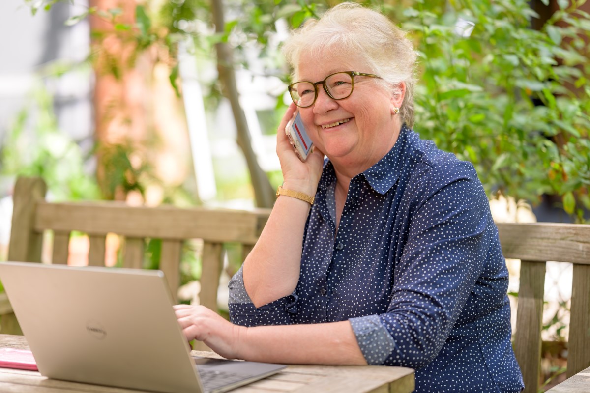 A senior woman on the phone while using a laptop.